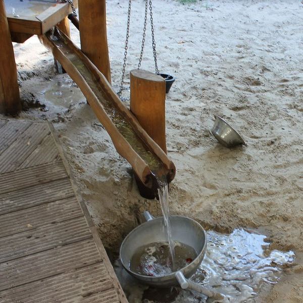 Wasser fließt durch Holzrinne in eine Schüssel